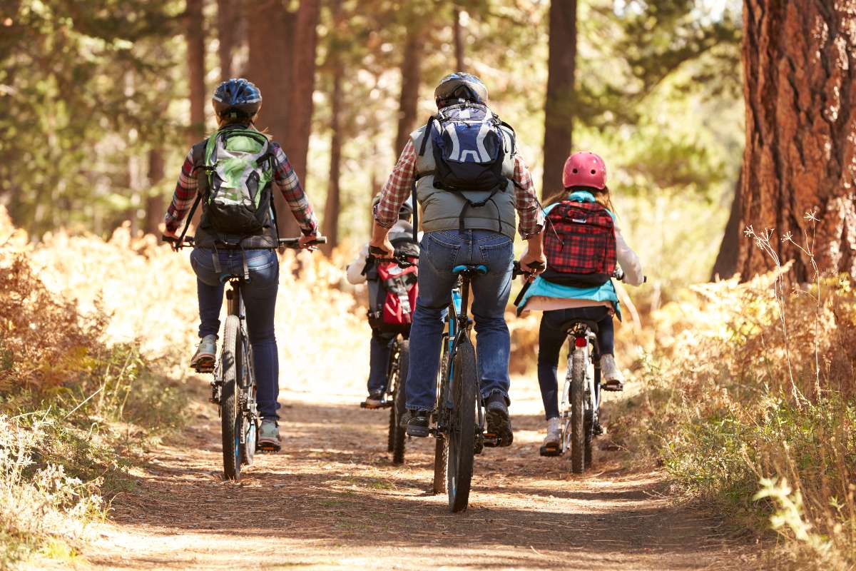 Famiglia che pedala insieme su un sentiero immerso in un bosco dai colori autunnali.