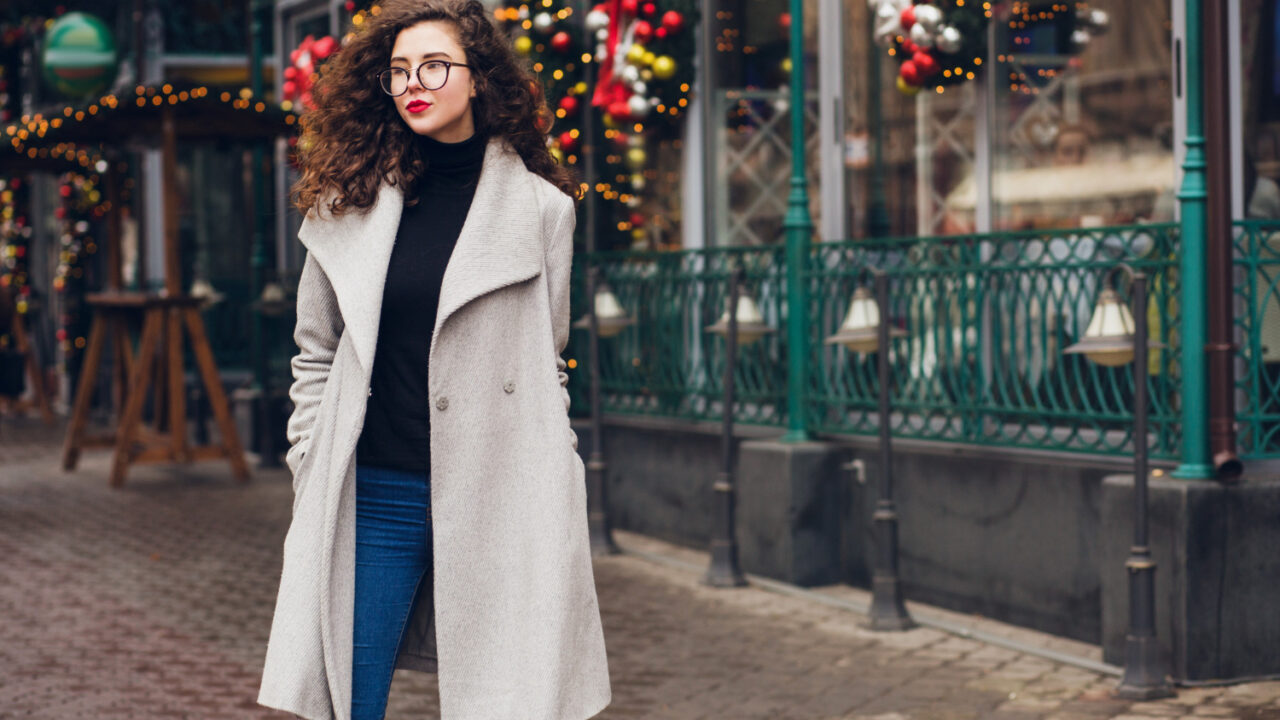 Look invernale: ragazza in cappotto grigio davanti a un locale addobbato per Natale.