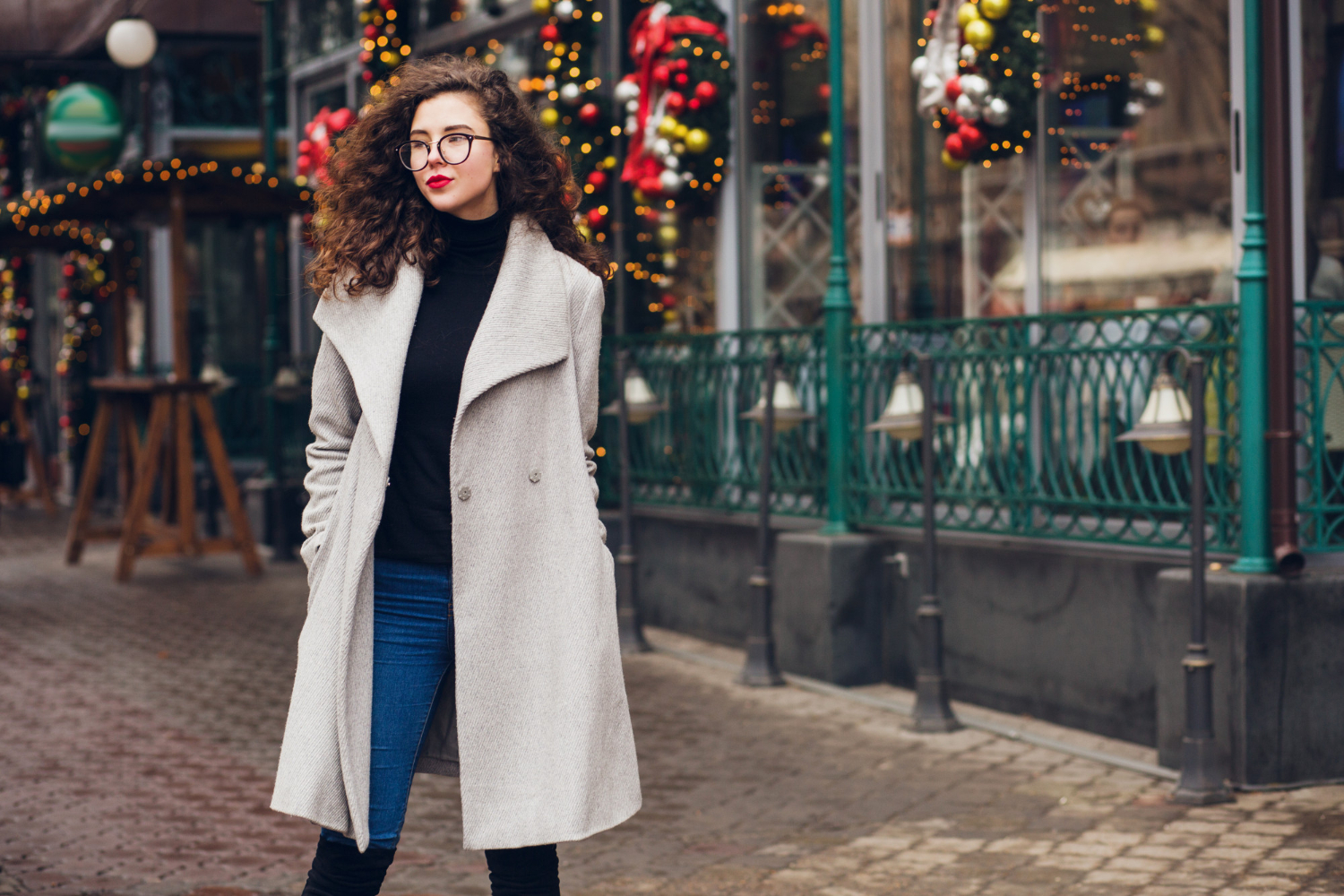 Look invernale: ragazza in cappotto grigio davanti a un locale addobbato per Natale.