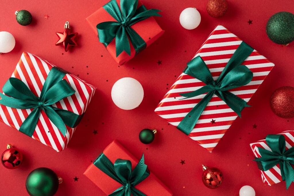 Composizione natalizia vista dall'alto: pacchetti e decorazioni su sfondo rosso.