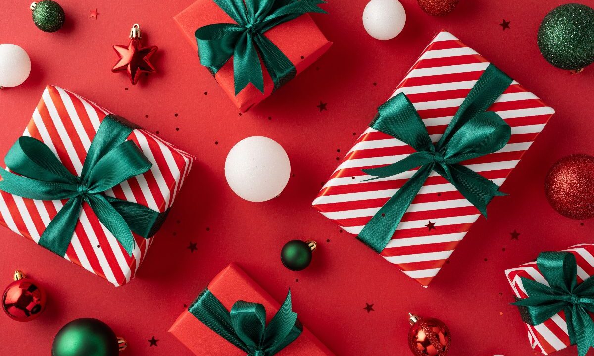 Composizione natalizia vista dall'alto: pacchetti e decorazioni su sfondo rosso.