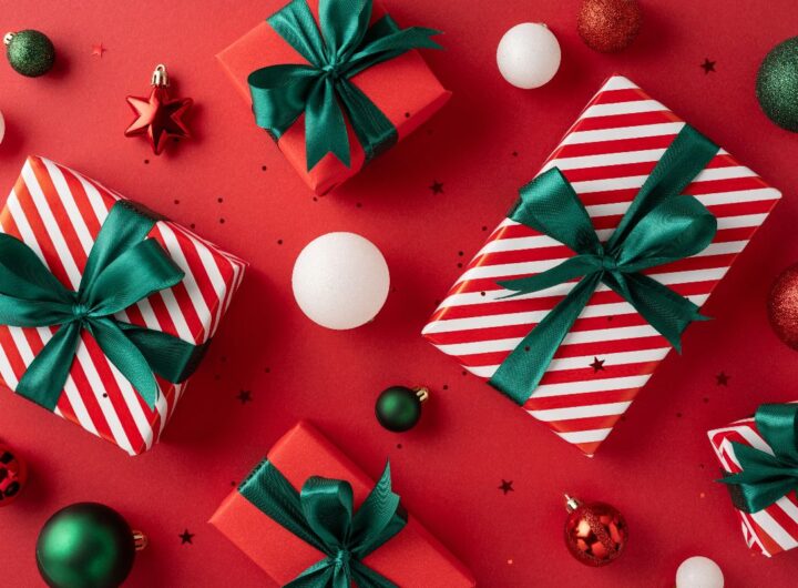 Composizione natalizia vista dall'alto: pacchetti e decorazioni su sfondo rosso.
