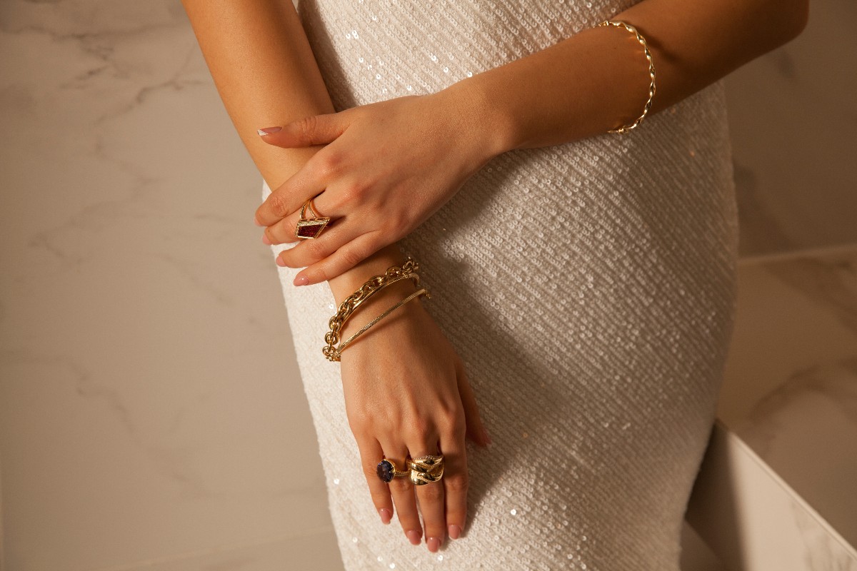 Dettaglio di mani femminili impreziosite da una serie di braccialetti e anelli in oro.
